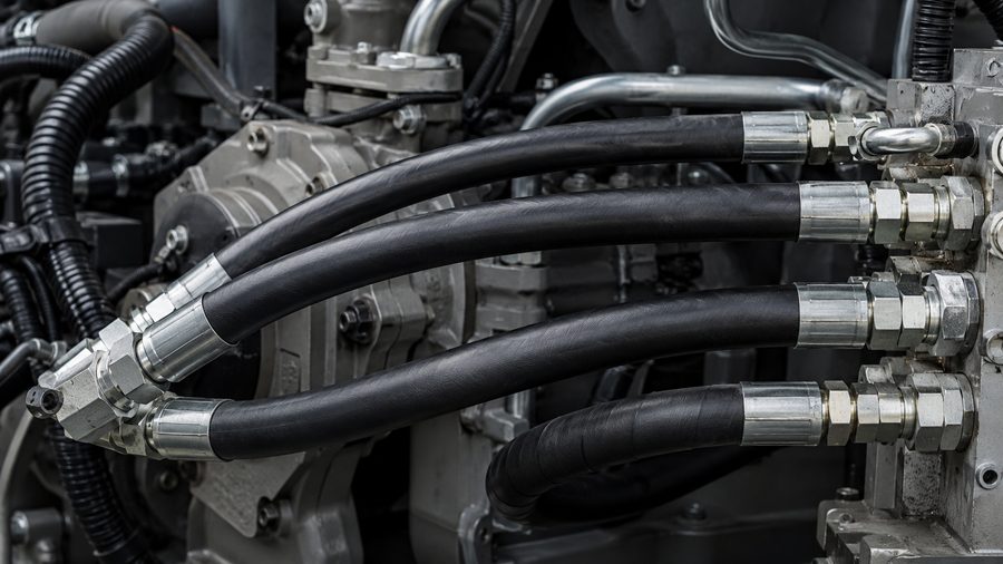 Black hydraulic hoses with crimped steel fittings connected to a machine manifold
